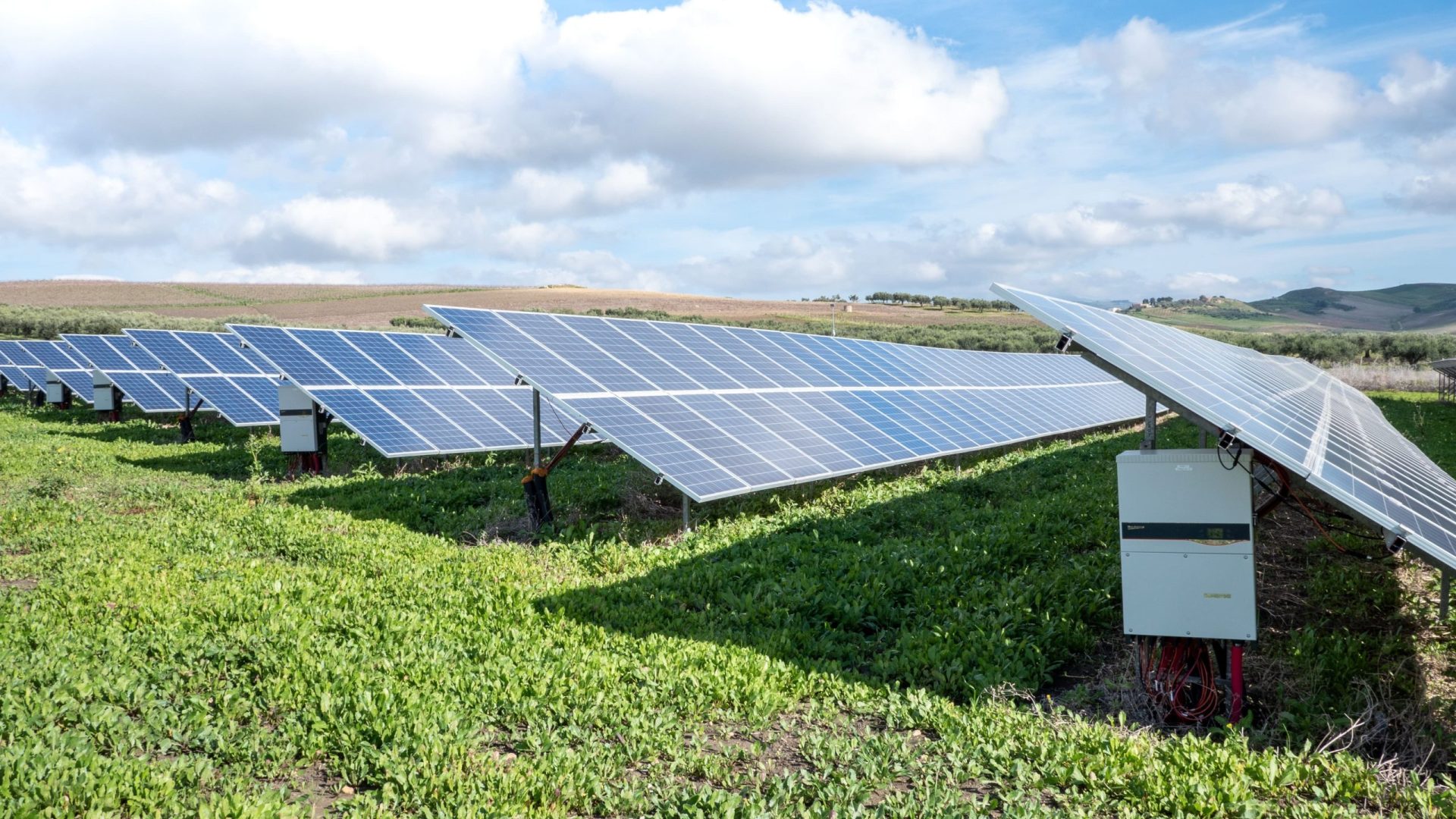 placas solares instaladas en mitad de un campo verde y un cielo despejado con sol